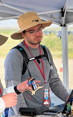 Ben standing in the New Mexico Desert looking at an electronic device used in the competition rocket, Blue Ridge Blazer